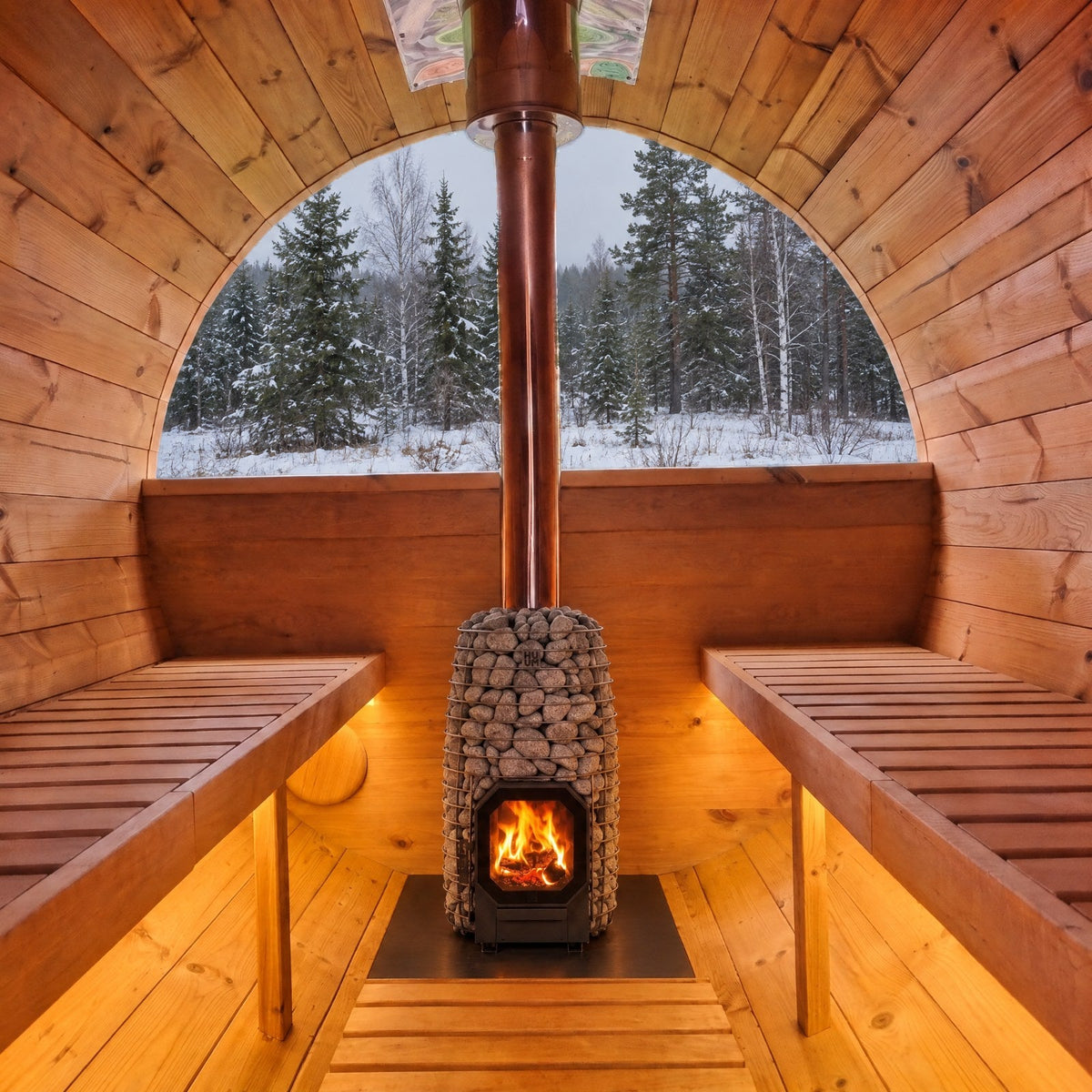 Fasssauna innen mit HUUM Hive Flow Holzofen auf Hitzeschutzplatte, LED unter den Bänken und Blick in den verschneiten Wald